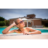 Young Beautiful Suntanned Woman wearing sunglasses relaxing next to a Swimming Pool  on a lovely Summer Day