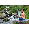 Woman meditating in Hatha yoga asana Padmasana outdoors at tropical waterfall
