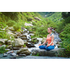 Woman in Hatha yoga asana Padmasana outdoors at tropical waterfall