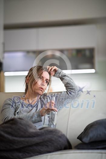 Midlle aged woman at home with a bottle of strong alcohol in her hands