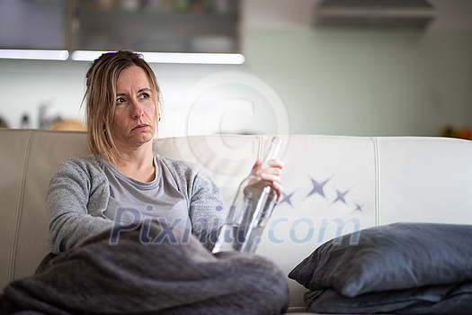 Midlle aged woman at home with a bottle of strong alcohol in her hands