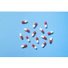 Red and white pharmaceutical capsules scattered over blue background, copy space. Health care and medication-assisted treatment.