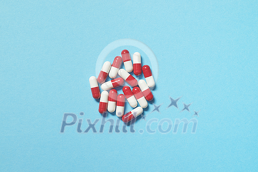 Red and white pharmaceutical tablets scattered over blue backdrop, copy space. Health care and medication-assisted treatment.