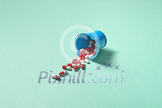 Pharmaceutical tablets falling out of bucket over touquose background. Flat lay with copy space.