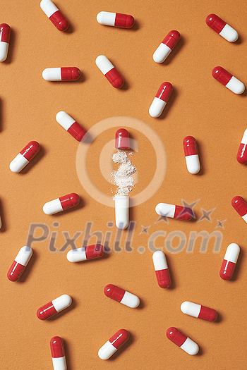 Pharmaceutical pills and medication powder scattered over orange background. Health care and medication-assisted treatment.