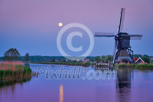 Netherlands rural lanscape with windmills at famous tourist site Kinderdijk in Holland in twilight with full moon