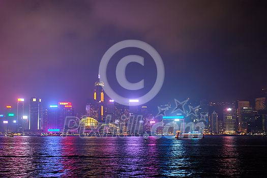 Hong Kong skyline cityscape downtown skyscrapers over Victoria Harbour in the evening illuminated with lasers with tourist boat ferries . Hong Kong, China