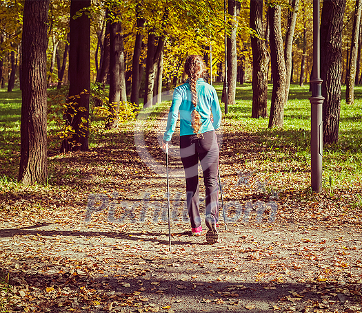 Vintage retro effect filtered hipster style image of nordic walking adventure and exercising concept - woman hiking with nordic walking poles in park