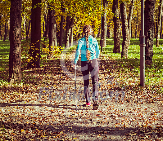 Vintage retro effect filtered hipster style image of nordic walking adventure and exercising concept - woman hiking with nordic walking poles in park Vintage retro effect filtered hipster style image of nordic walking adventure and exercising concept - woman hiking with nordic walking poles in park