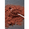 High angle of shiny spoon on heap of dry brown powder of Theobroma cocoa beans on gray surface