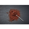 Top view of shiny spoon on piled of dark cocoa powder scattered on gray background