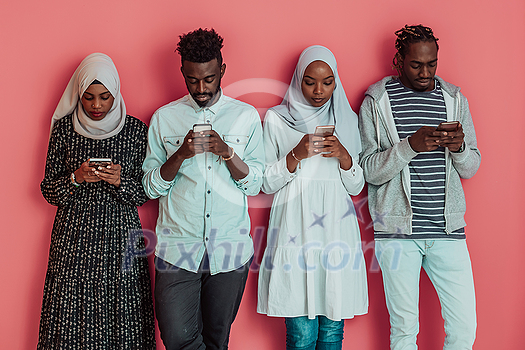 A group of African Muslim students using smartphones while standing in front of a pink background. High-quality photo