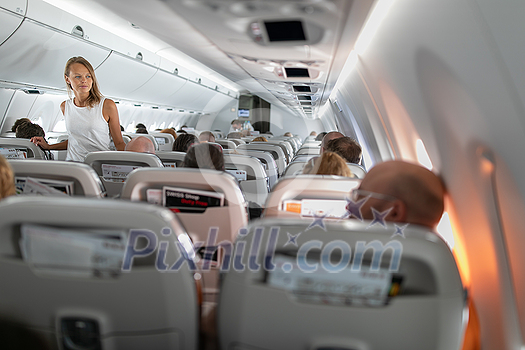 Pretty, young happy woman aboard an airplane during a lang haul commercial flight - stretching her legs a bit, walking in the aisle