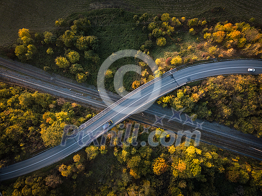 Winding road in autumn forest at sunset in mountains. Aerial view. Top view of beautiful asphalt roadway and orange trees. Highway through the woodland in fall. Trip in europe. Travel and nature Winding road in autumn forest at sunset in mountains. Aerial view. Top view of beautiful asphalt roadway and orange trees. Highway through the woodland in fall. Trip in europe. Travel and nature