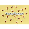 Hepatitis word formed of scrabble blocks and pharmaceutical pills scattered over yellow background. Liver disease and medical treatment concept.