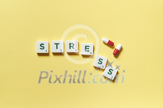 Stress word formed of scrabble tiles and pharmaceutical pills on yellow background. Mental health awareness.