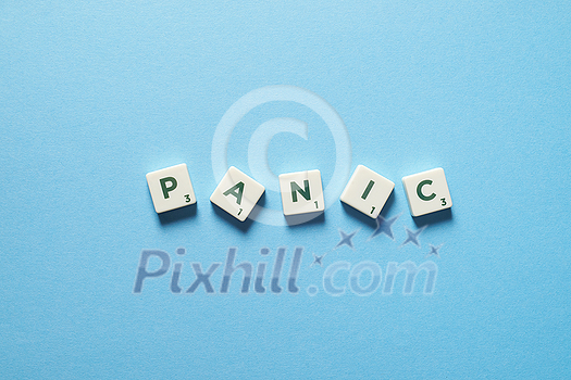 Panic word formed of messy scrabble tiles on blue backdrop. Anxiety and mental health awareness.