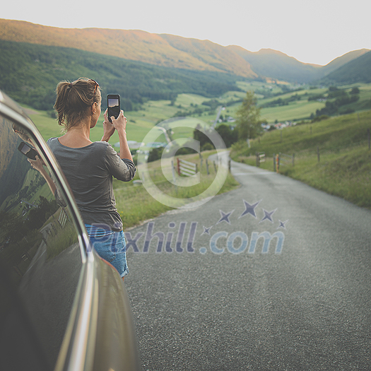 Traveling in nature, woman photographing alpine landscape with her smartphone
