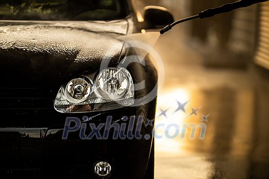 Young man washing his beloved car carefully in a manual car wash to prevent any damage and detail it properly Young man washing his beloved car carefully in a manual car wash to prevent any damage and detail it properly