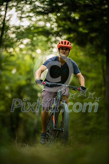 Young man with his mountain bike going for a ride past the city limits in a lovely forest, getting the daily cardio dose