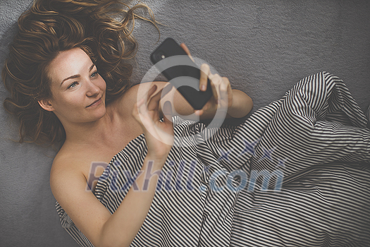 Pretty, young woman in her bed using her smart phone instead of relaxing Pretty, young woman in her bed using her smart phone instead of relaxing