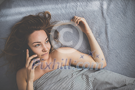 Pretty, young woman in her bed using her smart phone instead of relaxing