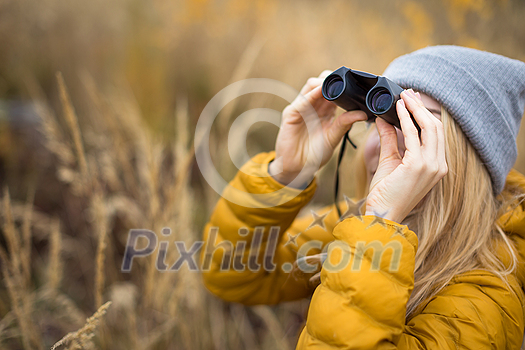 Young woman with binoculars outdoors on fall day. Enjoying the outdoors.