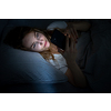 Young woman in bed holding a phone, tired and exhausted, blue light straining her eyes, messing up her circadian rhytm