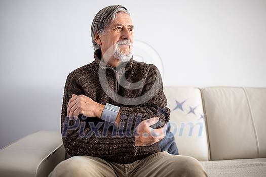 Senior man using medical device to measure blood pressure - elderly man suffering from high blood pressure sitting at home on sofa takes care of his health