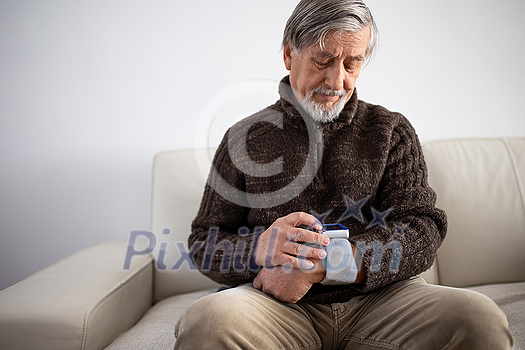 Senior man using medical device to measure blood pressure - elderly man suffering from high blood pressure sitting at home on sofa takes care of his health