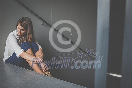 Depressed young woman sitting in a staircase, jobloss due to coronavirus pandemic, Covid-19 outbreak. Unemployment, economic crisis, financial distress concept