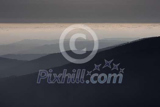 Mountain atmospheric landscape of high mountains in thick fog in rainy weather, panorama of mountain tops in thick clouds, dawn in the mountains in early spring.