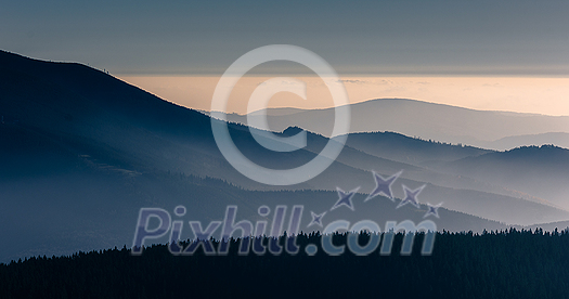 Mountain atmospheric landscape of high mountains in thick fog in rainy weather, panorama of mountain tops in thick clouds, dawn in the mountains in early spring.