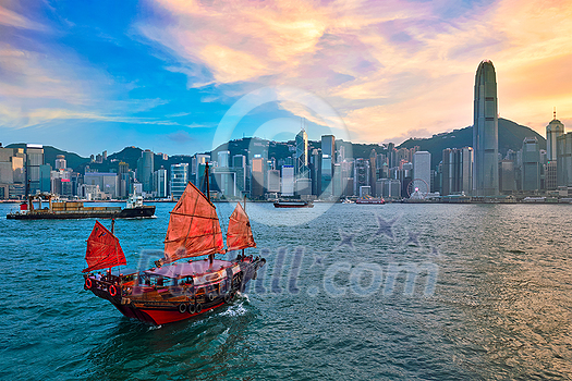 Hong Kong skyline cityscape downtown skyscrapers over Victoria Harbour in the evening with junk tourist ferry boat on sunset with dramatic sky. Hong Kong, China