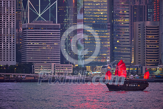 Tourist junk boat ferry with red sails and Hong Kong skyline cityscape downtown skyscrapers over Victoria Harbour in the evening. Hong Kong, China