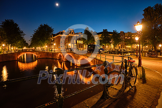 Night view of Amterdam cityscape with canal, bridge and medieval houses in the evening twilight illuminated. Amsterdam, Netherlands