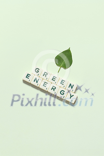 Green energy words formed of scrabble tiles with fresh tree leaf on light green background. Eco energy and natural resource conservation concept.
