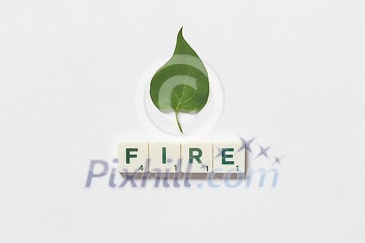 Fire word formed of scrabble tiles with green tree leaf on white background. Eco energy and natural resource conservation concept.