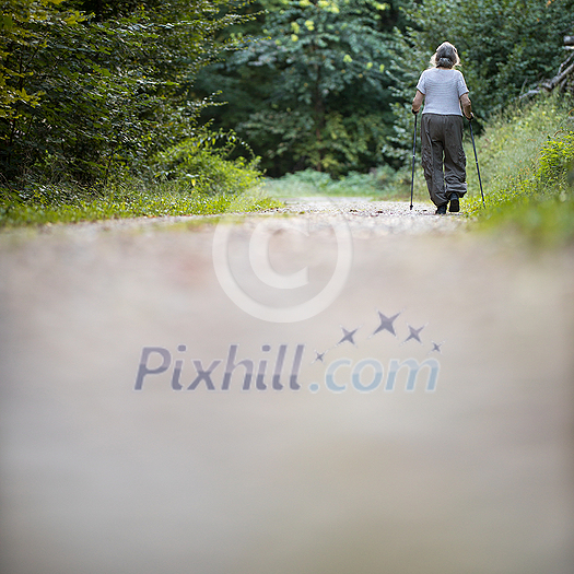Senior woman nordic walking on a forest path, getting in her daily cardio dose Senior woman nordic walking on a forest path, getting in her daily cardio dose