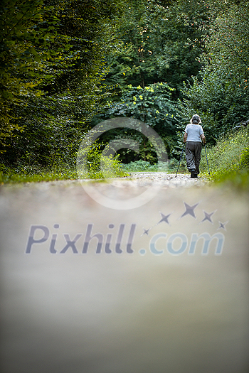 Senior woman nordic walking on a forest path, getting in her daily cardio dose Senior woman nordic walking on a forest path, getting in her daily cardio dose