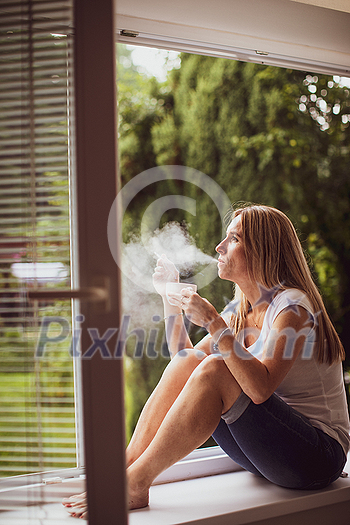 Mid-aged woman lighting a cigarette at home, getting her nicotine daily dose, unable to resist to her unhealthy habit Mid-aged woman lighting a cigarette at home, getting her nicotine daily dose, unable to resist to her unhealthy habit