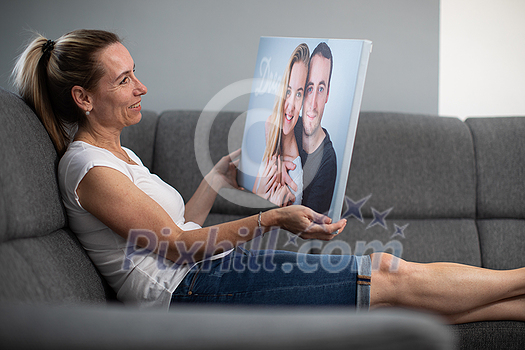 Mid-aged woman with a photo printed on a canvas in her hands. Portrait of her kids to be soon hanged on the wall.