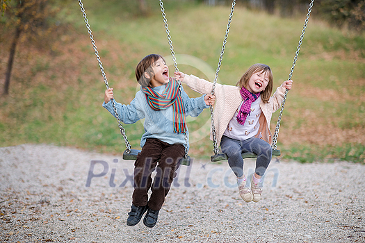 cheerful children are having fun on a swing little brother and sister playing outside