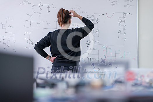 Young female student standing and writing on white chalkboard in a classroom Young female student standing and writing on white chalkboard in a classroom
