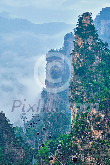 Famous tourist attraction of China - Zhangjiajie stone pillars cliff mountains in fog clouds with cable railway car lift at Wulingyuan, Hunan, China. With camera pan