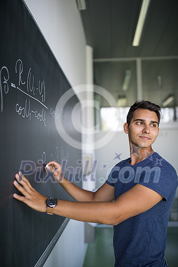 Students in a classroom - handsome student solving a math problem on a blackboard during math class Students in a classroom - handsome student solving a math problem on a blackboard during math class