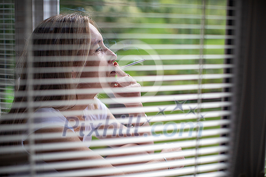 Mid-aged woman lighting a cigarette at home, getting her nicotine daily dose, unable to resist to her unhealthy habit Mid-aged woman lighting a cigarette at home, getting her nicotine daily dose, unable to resist to her unhealthy habit