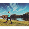 Vintage retro effect filtered hipster style image of nordic walking adventure and exercising - young woman hiking with nordic walking poles in park along river