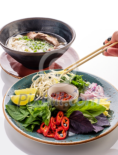 Traditional Japanese soup ramen with noodles and beef. Preparation of soup Ramen. A woman's hand puts herbs in a bowl of soup. Traditional Japanese soup ramen with noodles and beef. Preparation of soup Ramen. A woman's hand puts herbs in a bowl of soup.