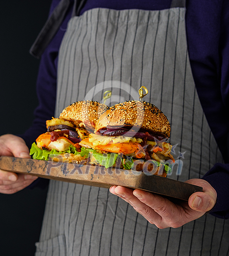 Chicken burger with pineapple. Men's hands hold a tray with a cheeseburger. Chicken burger with pineapple. Men's hands hold a tray with a cheeseburger.
